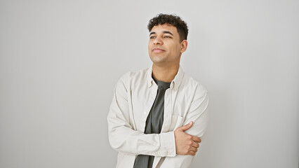 Confident young man with curly hair standing against a white wall, wearing a casual jacket and...