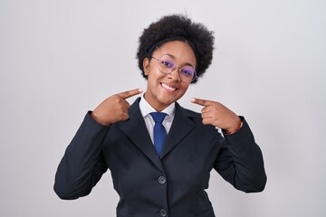 Beautiful african woman with curly hair wearing business jacket and glasses smiling cheerful showing and pointing with fingers teeth and mouth. dental health concept.