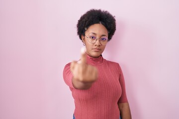 Beautiful african woman with curly hair standing over pink background showing middle finger,...