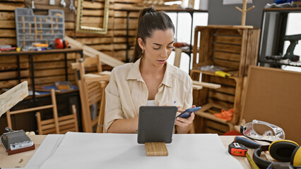 Radiant young hispanic woman, a professional carpenter, engaging with the digital world on her...
