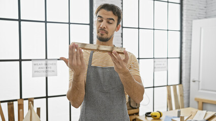 Handsome hispanic man inspecting wood in a well-lit carpentry workshop, conveying craftsmanship and...