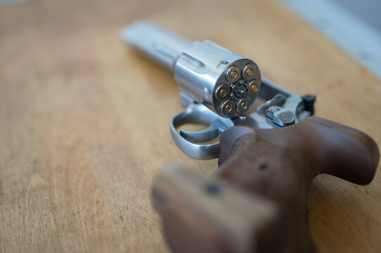 Detail of the drum of a revolver loaded with bullets. There is a lot of bokeh and the gun is on a wooden table. Caliber 357 magnum or .38 special