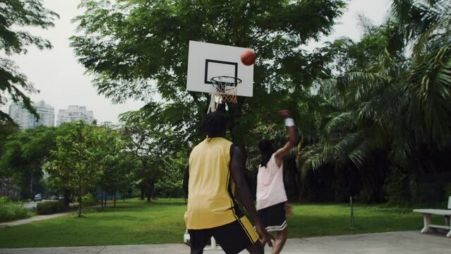 Handheld shot of two black sportsmen playing streetball while spending weekend on outdoor playground in city park