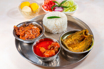 Bengali non vegetarian food thali comprising of plain white rice with spicy chicken curry, prawn and fish dishes, along with dessert and salad.