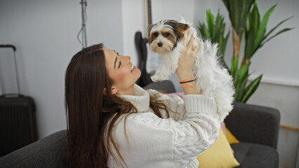 A smiling young hispanic woman enjoys quality time indoors with her beautiful biewer yorkshire terrier at home.