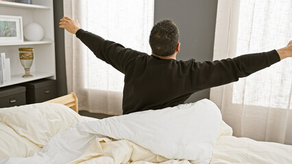 A young man stretches upon waking in a well-lit, cozy bedroom setting, exuding a sense of morning...