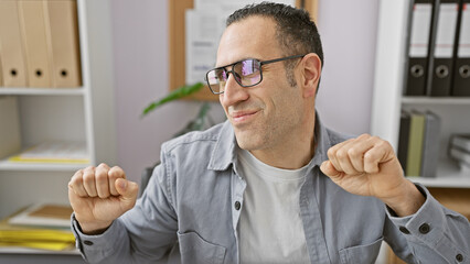 Smiling man with glasses stretching in a modern office, portraying relaxation during a workday.