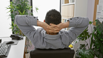 A relaxed hispanic man stretches in an office, exuding calmness and professional satisfaction.