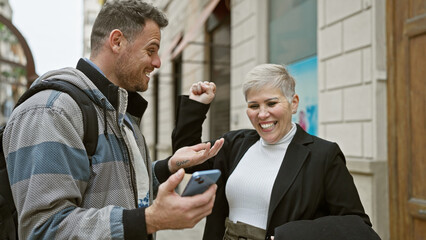 A happy man and woman interacting on a bustling city street, with the man holding a smartphone and both showing joyful expressions.