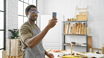 Young african american man taking a selfie in a modern carpentry workshop