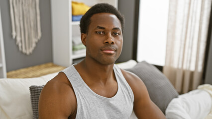 Portrait of a young african american man relaxed in a modern bedroom setting, looking at the camera.