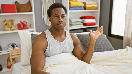 Adult african american man sitting in bed with a questioning expression in a modern bedroom...