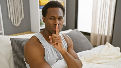 Young adult african american man gesturing silence in a well-lit cozy bedroom - obrazy, fototapety, plakaty