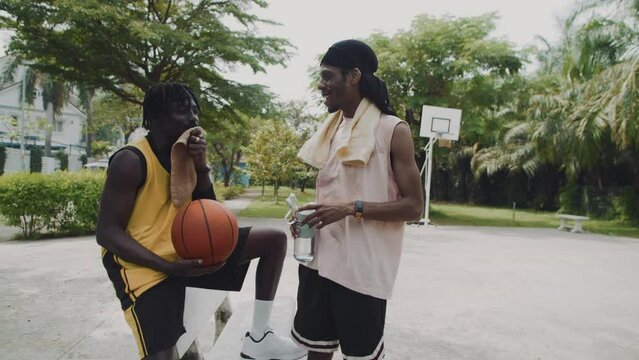 Medium long shot of two black male basketballers chatting while resting outdoors after training