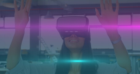 Image of blue and pink light trails moving over biracial woman wearing vr headset at office - Powered by Adobe