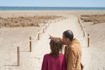Mature couple in path to the beach pointing at sea