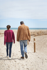 Vertical shot of mature couple in beach sand path walking to the sea