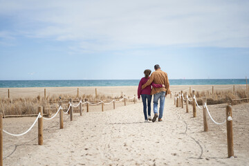 Mature couple in beach sand path walking to the sea
