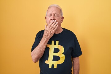 Senior man with grey hair wearing bitcoin t shirt bored yawning tired covering mouth with hand....