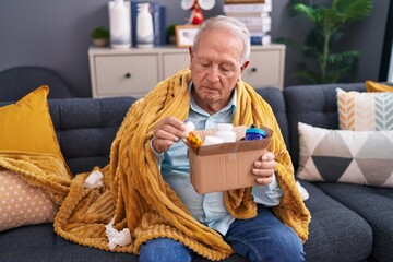 Middle age grey-haired man holding pills of delivery package sitting on sofa at home