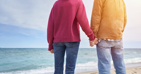 Mature couple holding hands in the beach and looking at the ocean