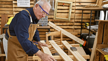 Relaxed and serious mature man, a professional carpenter, sanding a plank of wood at his carpentry...