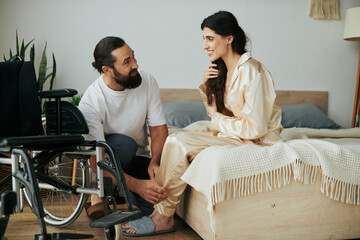 bearded loving man in homewear helping his disabled wife to change into pajama in bedroom at home - obrazy, fototapety, plakaty