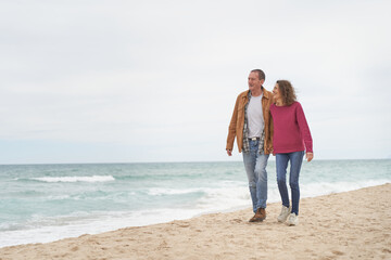 Mature Couple walking in beach sand by the ocean