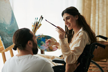 caring jolly husband helping his inclusive good looking wife to paint on easel while at home - obrazy, fototapety, plakaty