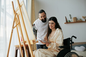 attractive bearded man watching his disabled beautiful wife on wheelchair painting on easel at home