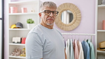 Mature grey-haired man in glasses standing in a pastel-colored dressing room, looking at the camera.