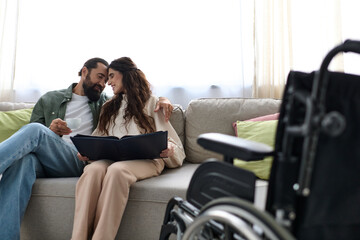 joyous bearded man spending quality time at laptop with his disabled beautiful wife, drinking coffee