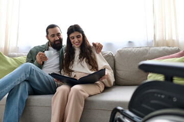 joyous bearded man spending quality time at laptop with his disabled beautiful wife, drinking coffee