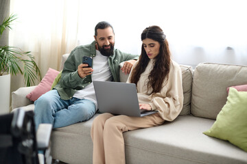 beautiful woman with mobility disability sitting on sofa with laptop next to her husband with phone