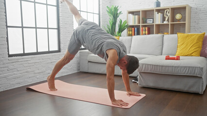 A fit man practices yoga indoors, balancing in a challenging posture on a mat in a bright, modern...