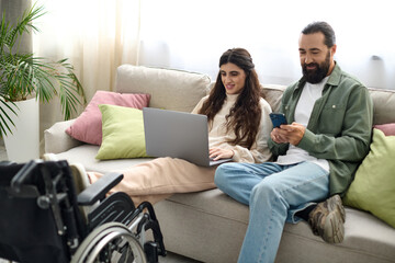 beautiful woman with mobility disability sitting on sofa with laptop next to her husband with phone - obrazy, fototapety, plakaty