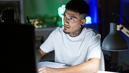 Serious young latin man, a tattooed musician artist, deep into composing song notes in his night...