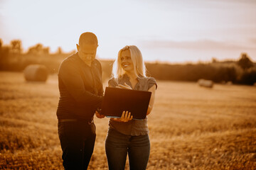 Valmiera, Latvia - August 17, 2024 - Two professionals look at a laptop together in a harvested...