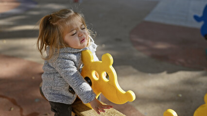Blonde little girl playing on a yellow animal spring rider in the park - Powered by Adobe