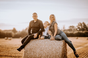 Valmiera, Latvia - August 17, 2024 - A family is sitting closely together on a hay bale in a field;...