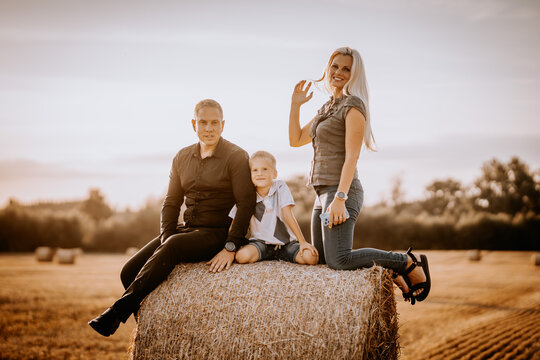 Valmiera, Latvia - August 17, 2024 - A family with a boy sitting on a hay bale in a field during sunset, the woman is waving.
