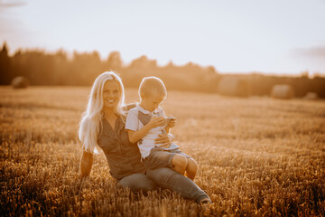 Valmiera, Latvia - August 17, 2024 - A mother and her son sit in a field at sunset, with the boy...
