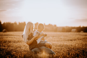 Valmiera, Latvia - August 17, 2024 - A mother and son are engaged with a smartphone in a sunlit field, the boy concentrating on the screen. - obrazy, fototapety, plakaty