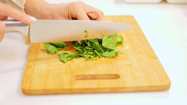 Sharp knife swiftly cuts through fresh greens on board. With each movement knife expertly slices greens creating captivating culinary scene. Sound of knife against board adds to mesmerizing atmosphere