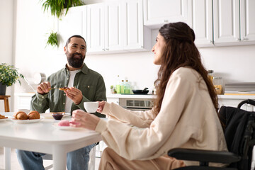cheerful woman with inclusivity in wheelchair eating sweets at breakfast with her handsome husband