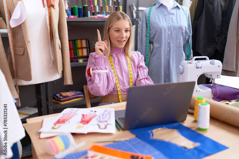 Wall mural young caucasian woman dressmaker designer using laptop smiling with an idea or question pointing fin