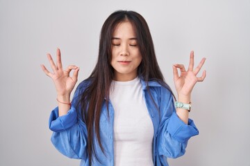 Young chinese woman standing over white background relaxed and smiling with eyes closed doing meditation gesture with fingers. yoga concept.