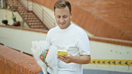 Young, confident caucasian man with his happy pet dog, smiling, sitting on a bench in the city;...