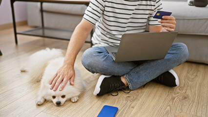 Young caucasian man with dog using laptop and credit card sitting on sofa at home