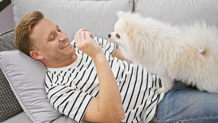 Confident young caucasian man joyfully relaxing on sofa with his happy dog, the person's cheerful...